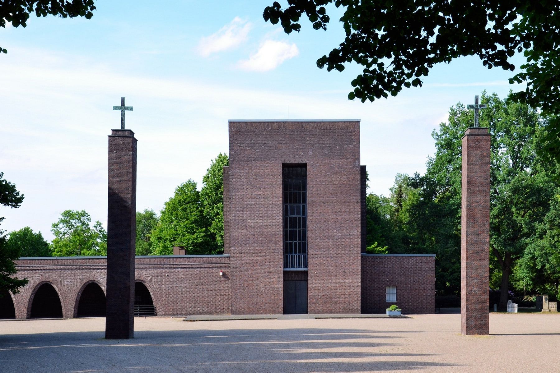 Symmetrische Frontansicht der roten Backstein-Trauerhalle mit hohem Mittelbau, Rundbogenarkaden und zwei freistehenden Kreuzpfeilern auf Südwestfriedhof Essen