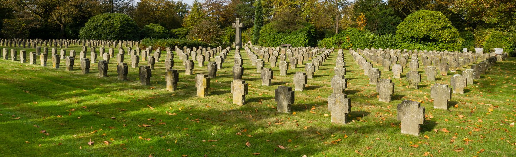 Ein breites Ehrenfeld mit regelmäßig gesetzten kleinen Steinkreuzen auf grünem Rasen führt zu einem hohen zentralen Kreuz, eingefasst von Bäumen und Hecken. auf Südwestfriedhof Essen